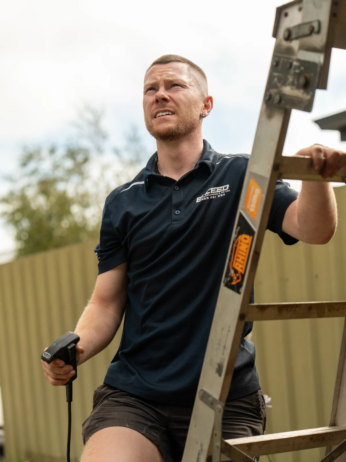 Technician on a ladder with a drill during an air conditioning installation